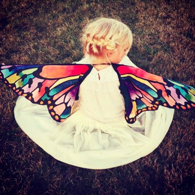 Kid wearing rainbow butterfly wings she colored in herself courtesy of Seedling.com.